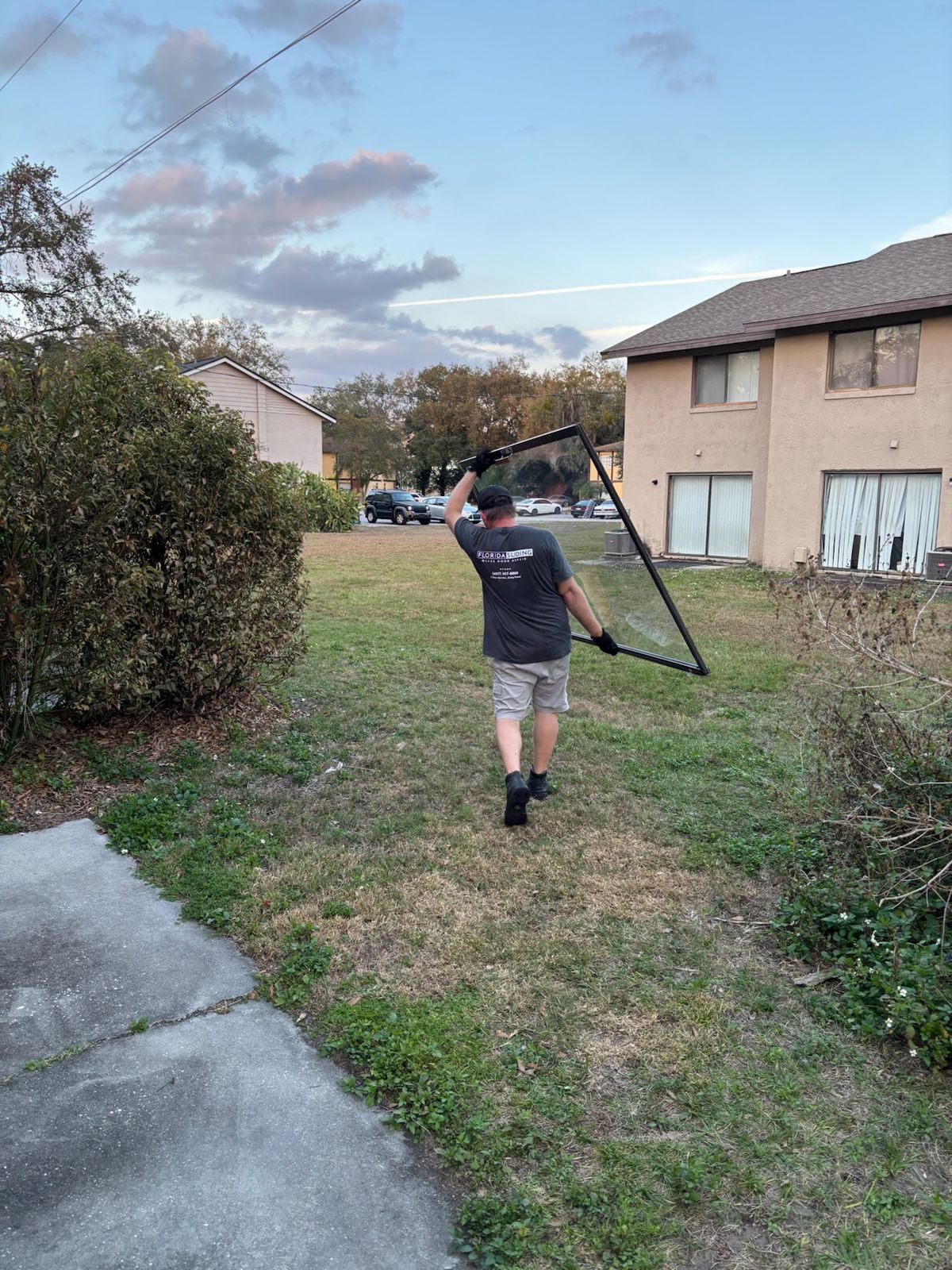 Technician carrying a sliding glass door frame across a yard — sliding glass door repair in Gainesville, Florida