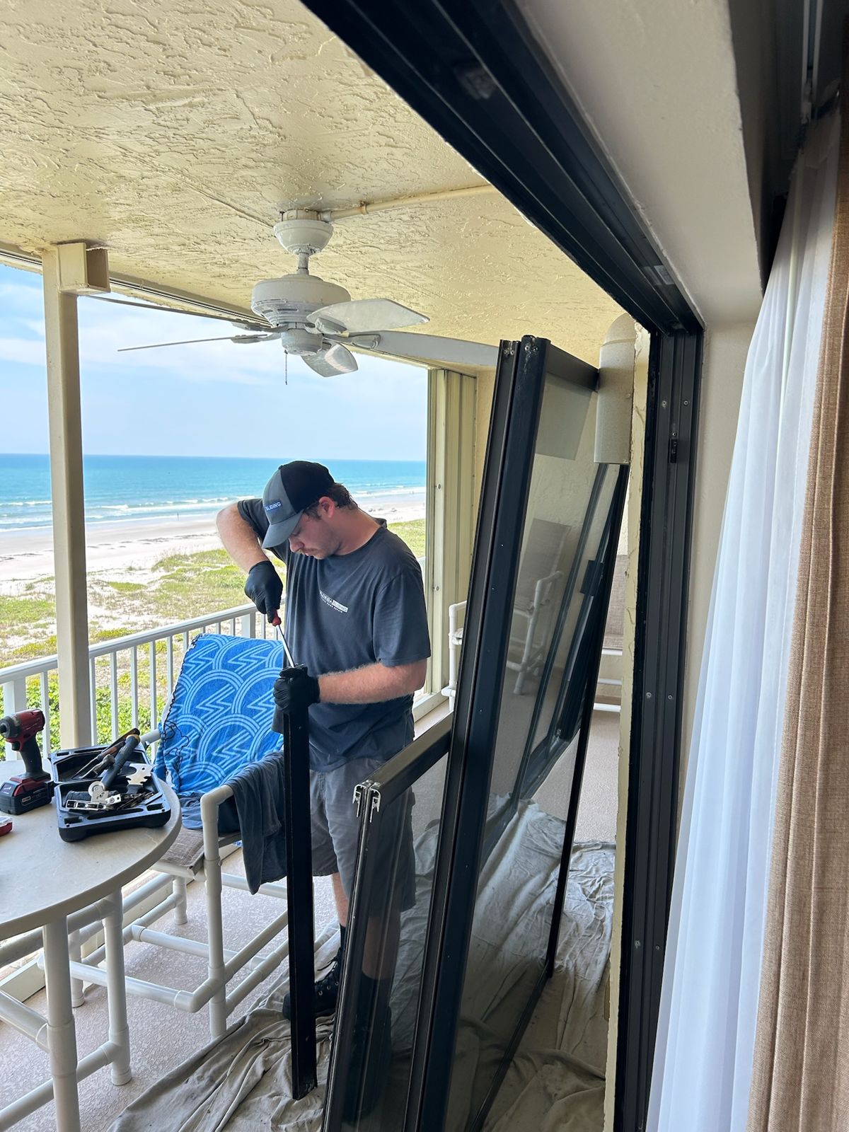 Technician carrying a sliding door panel on an oceanfront patio — sliding glass door services in Cocoa, Florida